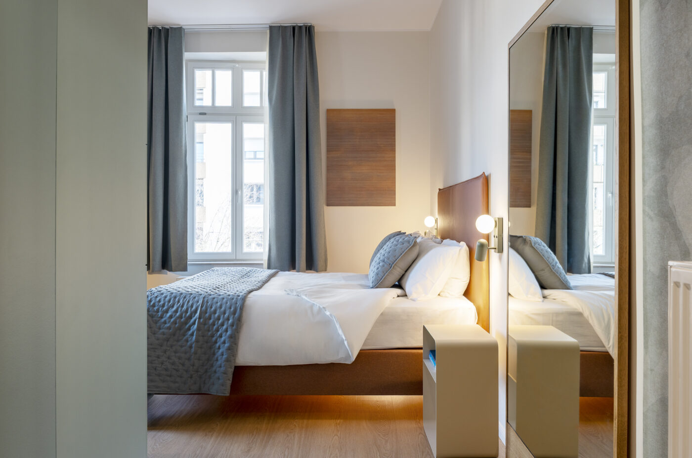 Keyinn Serviced Residences Belair bedroom with a bed, headboard, lamp, and mirror. The space includes a window and curtains.