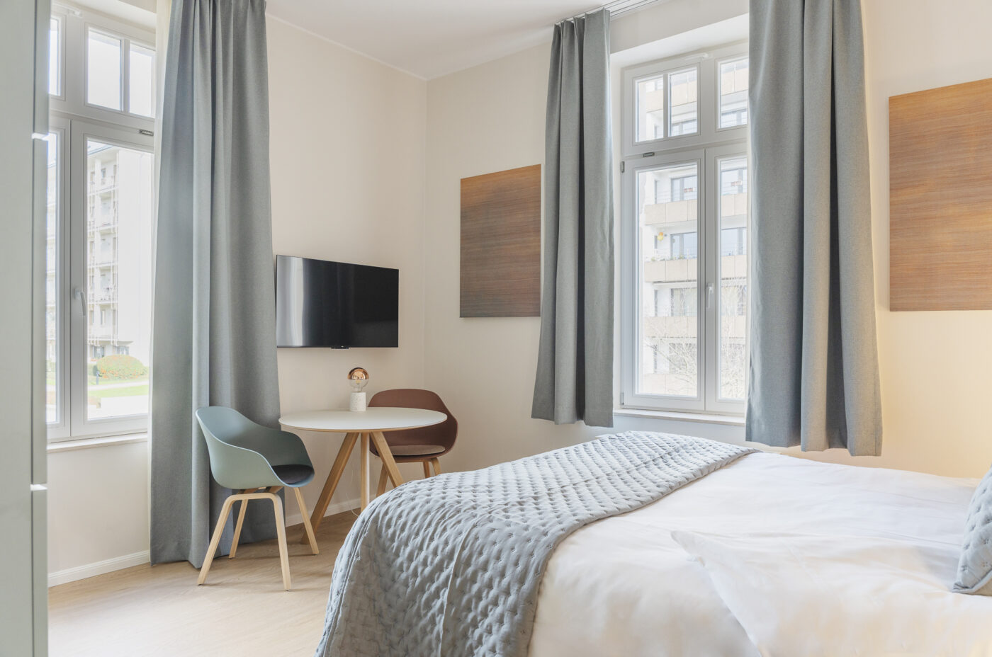 Keyinn Serviced Residences Belair bedroom with a bed, windows, curtains, and wall panels. The space includes a table, chairs, and TV.
