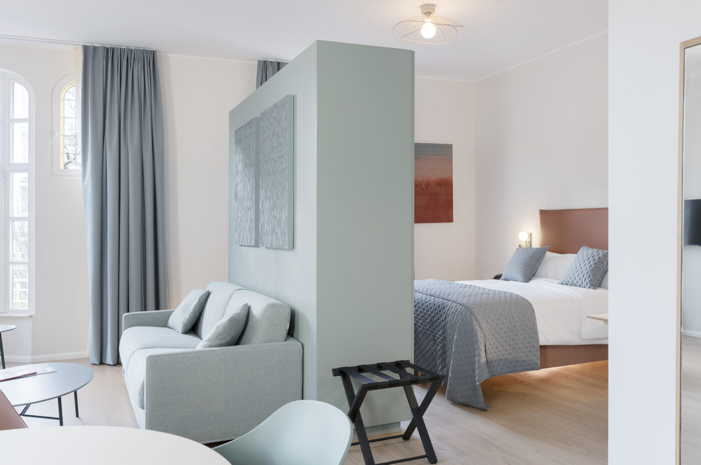 Keyinn Serviced Residences Belair room with a gray sofa, a dining table, and a stylish room partition. The space includes a separate bed with grey bedding and an elegant, modern design.