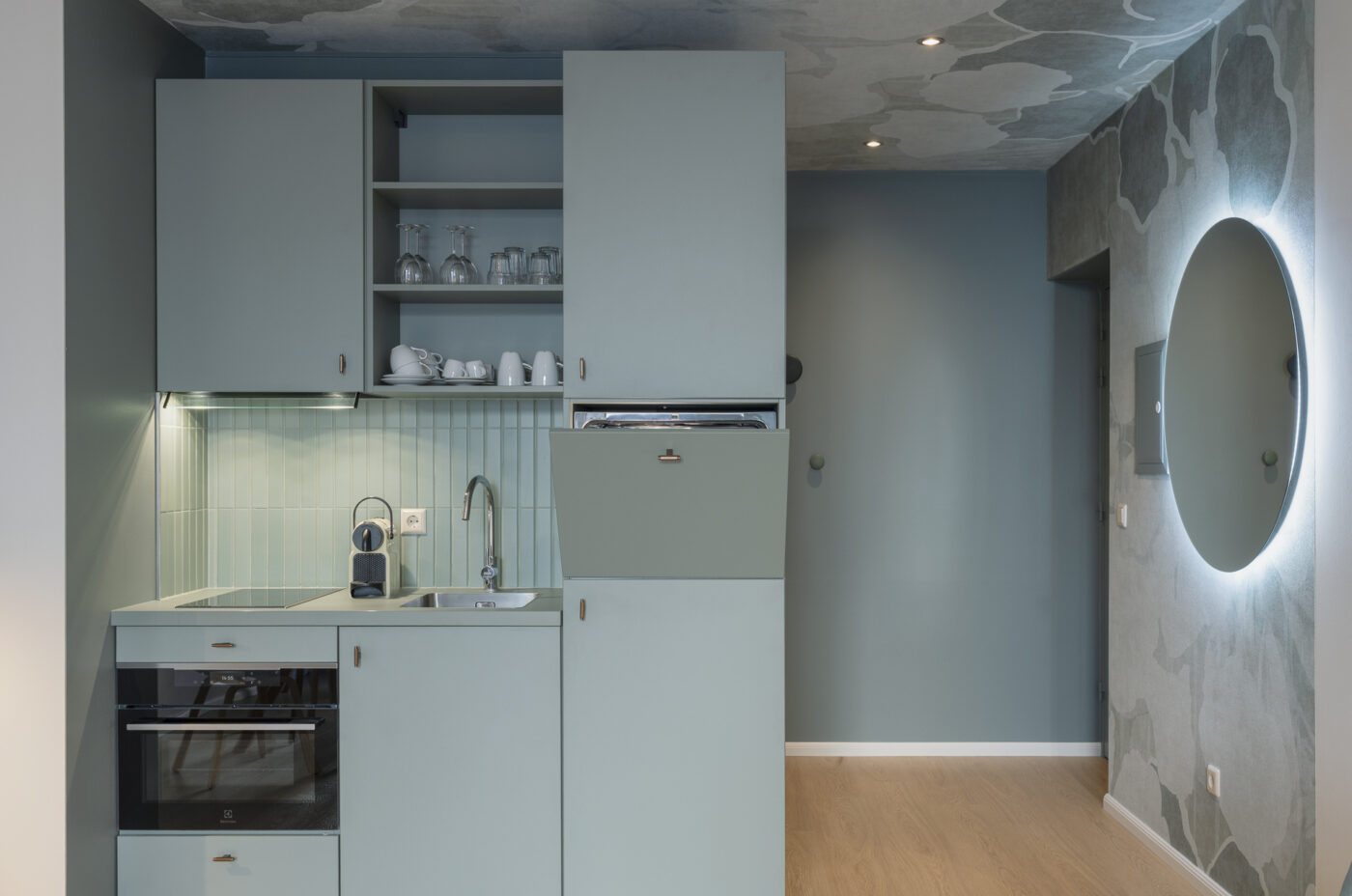 Keyinn Serviced Residences Belair kitchen with pastel blue cabinets, a built-in oven, and a sink. The space includes open shelving, glassware, and a minimalist design.
