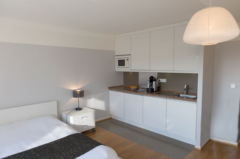 Keyinn Serviced Residences apartment. The space includes a bed & night stand on the left, & a compact kitchenette with white cabinets, a microwave, and a coffee maker on the right.