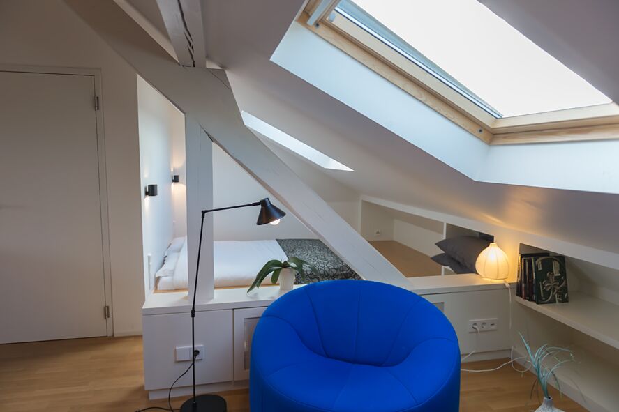 Keyinn Serviced Residences Parc de Merl bedroom with a sculptural slanted ceiling, skylight, and blue seating.