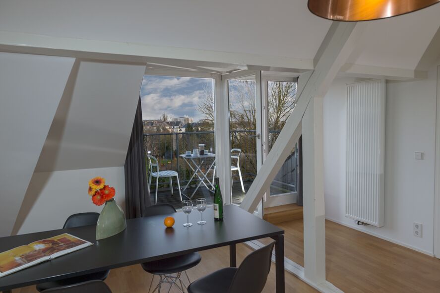 Keyinn Serviced Residences Parc de Merl dining space with a black table, a small floral arrangement, and a city-view balcony.