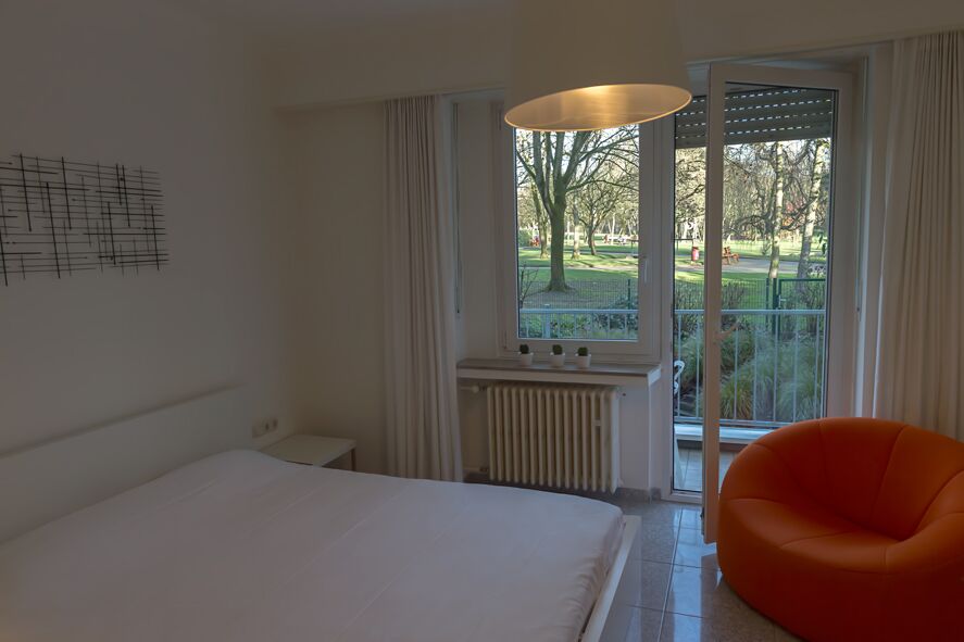 Keyinn Serviced Residences Parc de Merl room with a white bold orange seating, and an open window overlooking the park.