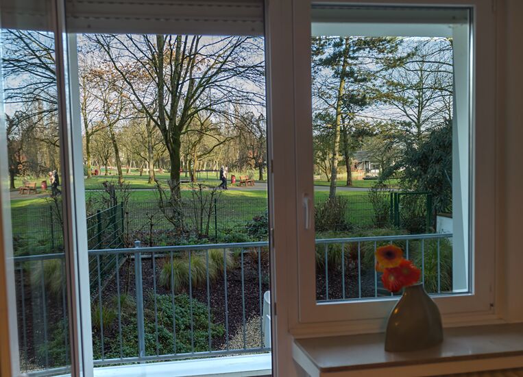 Keyinn Serviced Residences Parc de Merl window view featuring a floral arrangement set against a clear, sun-lit park.