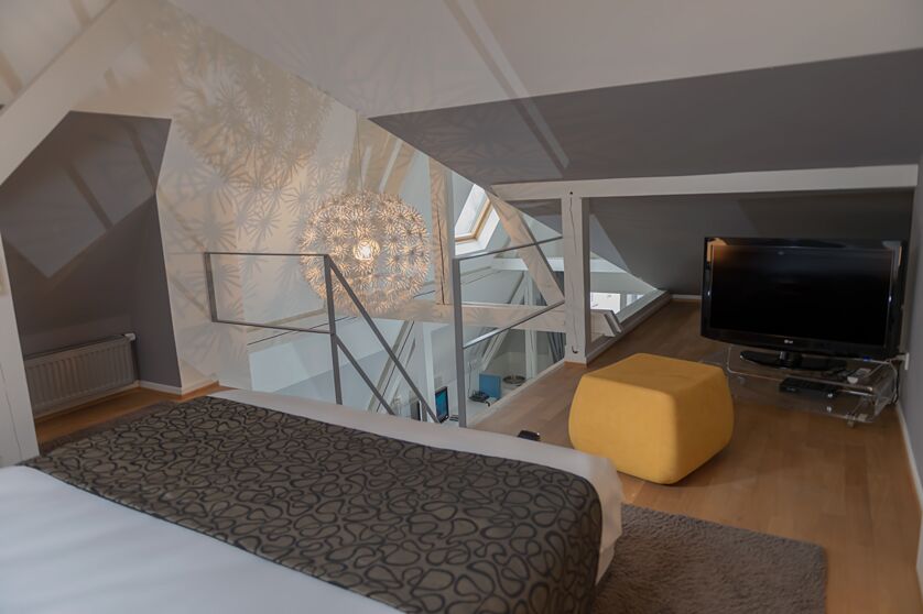 Keyinn Serviced Residences loft in Limpertsberg. With a patterned linen bed, a bold yellow ottoman, A flat-screen TV and a spherical light fixture.
