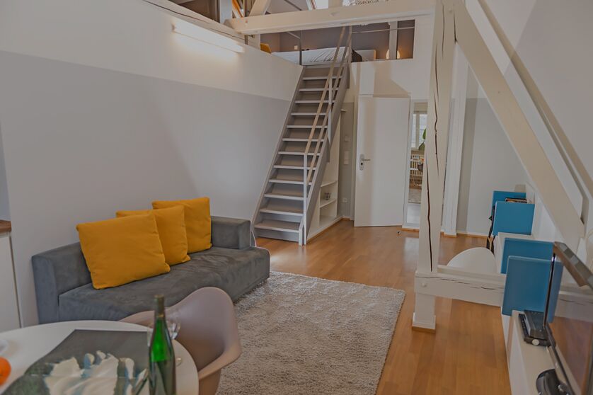 Keyinn Serviced Residences loft in Limpertsberg, with a grey and yellow seating area, wooden floors, and a staircase leading to a first floor bedroom.