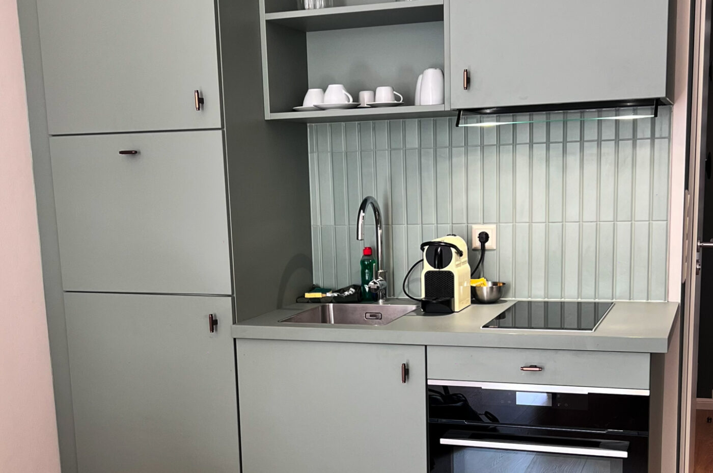 Keyinn Serviced Residences Belair kitchen with green cabinets, tiled backsplash, and modern appliances. The space includes a sink, coffee maker, oven, and organised shelving.