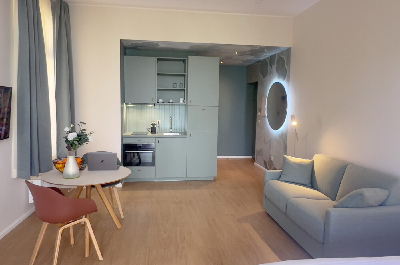 A KeyInn Services Residence apartment featuring a kitchenette, dining table, cozy sofa, and decorative wall with soft natural lighting.