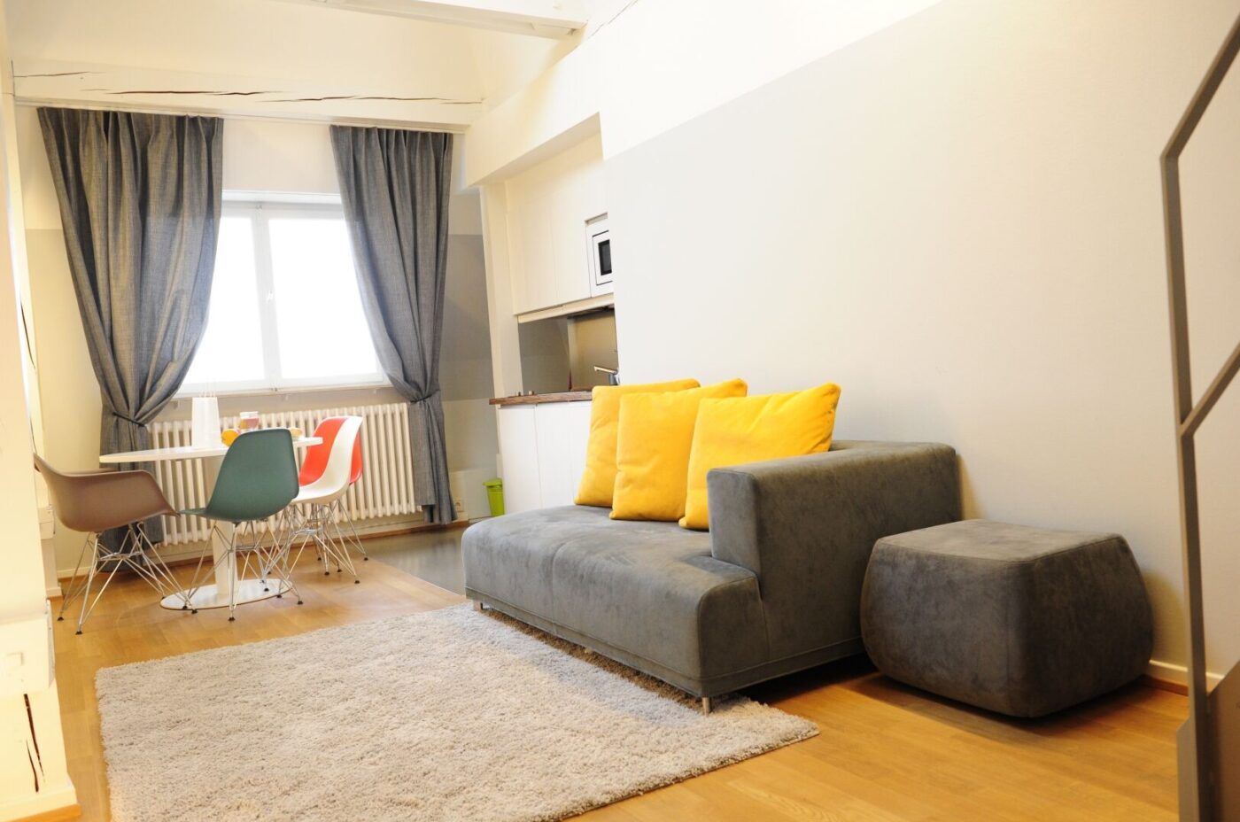 Keyinn Serviced Residences open-plan apartment in Limpertsberg with a grey and yellow seating area, vibrant dining chairs, and a plush rug.