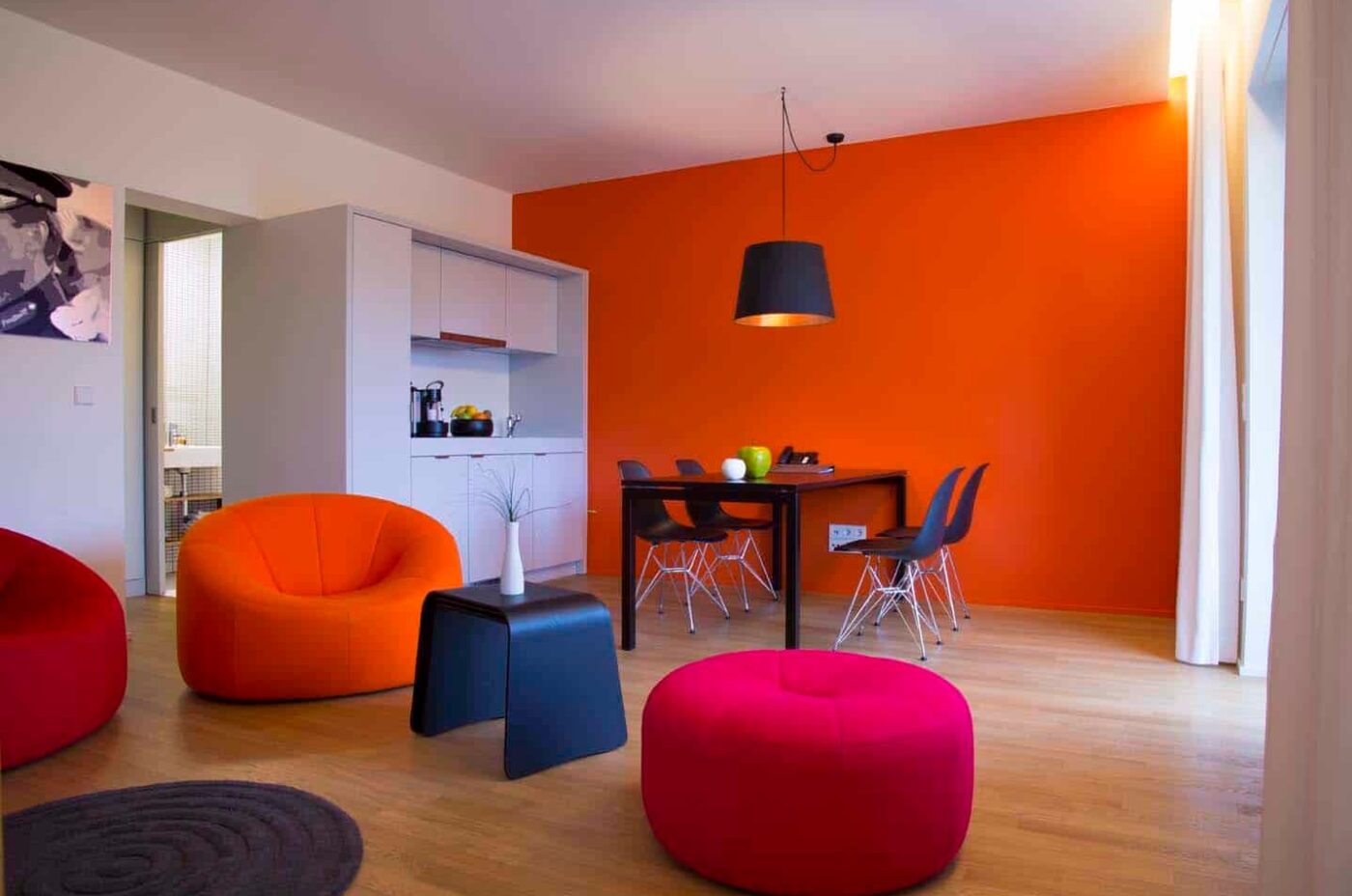 Keyinn Serviced Residences Parc de Merl living room with an orange wall, colourful seating, and a black dining table.