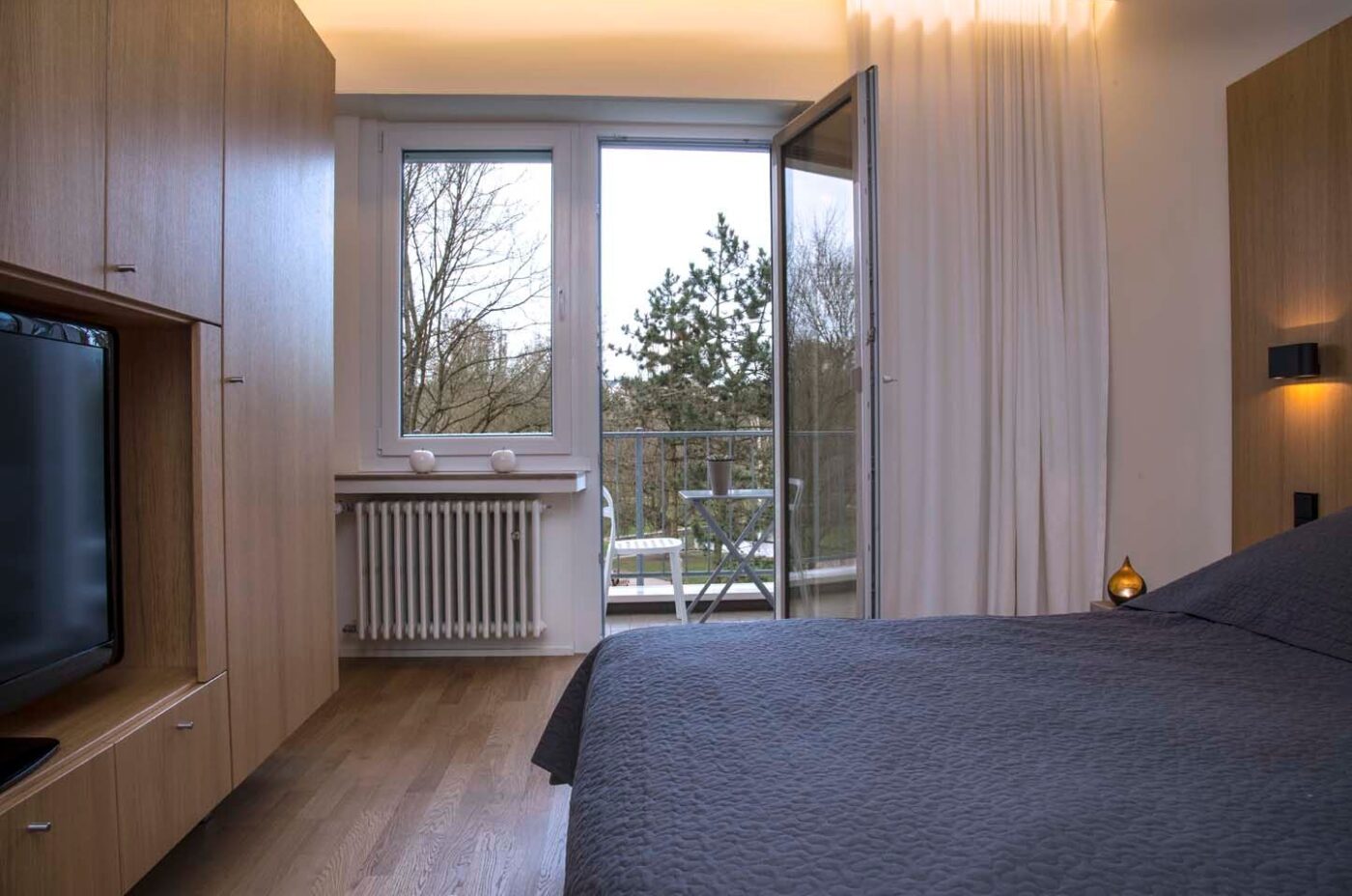 Keyinn Serviced Residences Parc de Merl bedroom with wood-panelled storage, double bed with a TV & adjoining balcony.