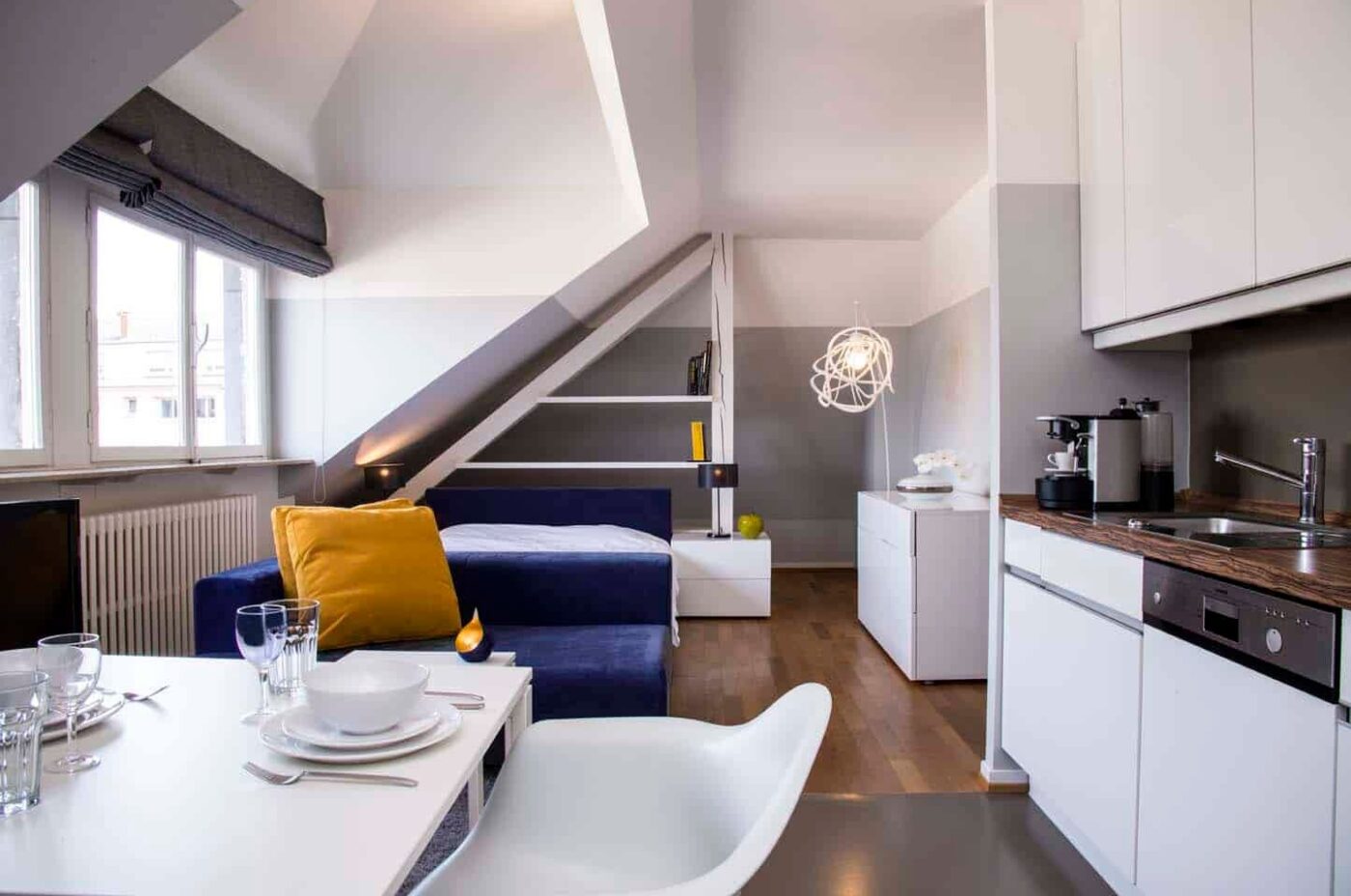 Keyinn Serviced Residences studio with a sloped ceiling, featuring a blue sofa, white kitchen, and dining area.