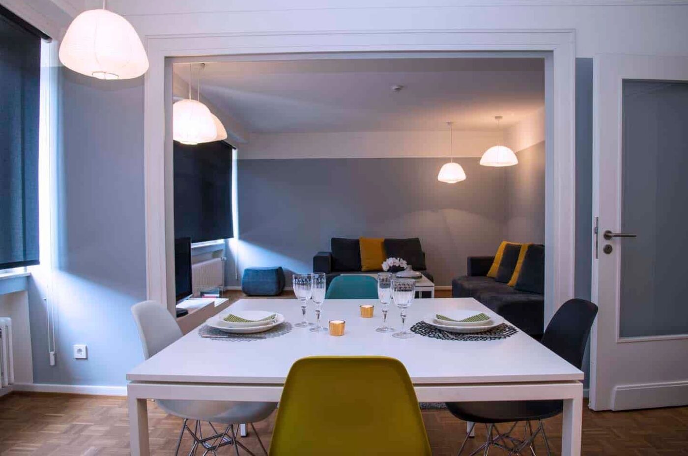 Keyinn Serviced Residences Limpertsberg open-plan area with a white dining set, bold seating, and plush gray sofas. Large pendant lights are furnished across the room.