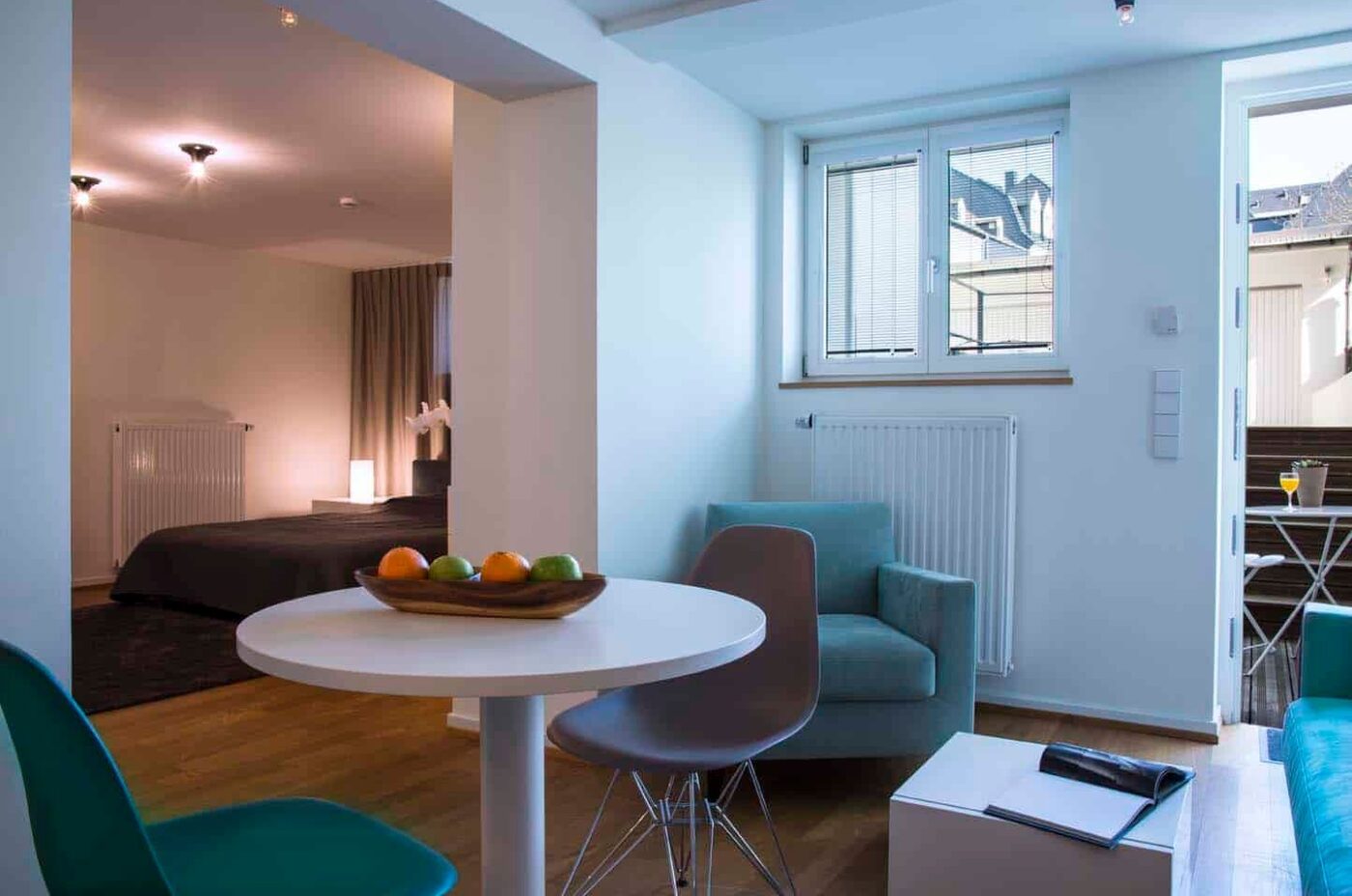 Keyinn Serviced Residences living space in Limpertsberg, with a round dining table, fruit bowl, and sleek chairs and a bedroom in the corner.