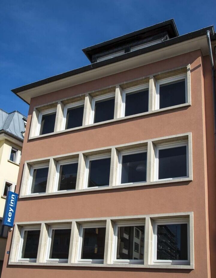 The Keyinn Serviced Residences Building in Limpertsberg. Styled with a brown facade and rows of square windows, under a clear blue sky.