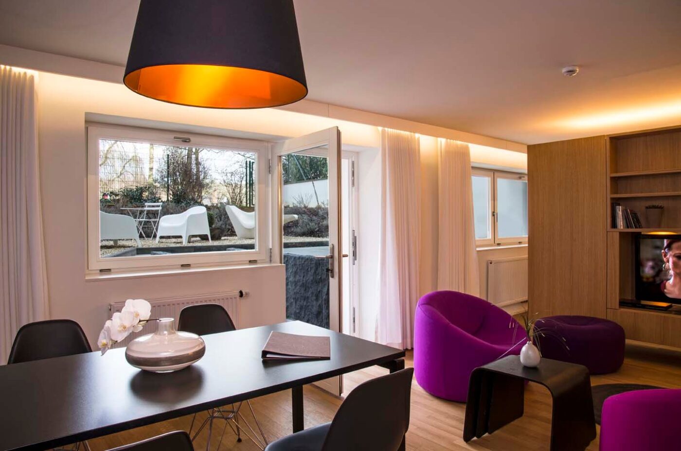 Keyinn Serviced Residence in Parc de Merl featuring a black dining table, purple chairs, and garden views. Warm illumination and a sophisticated layout create a welcoming feel.